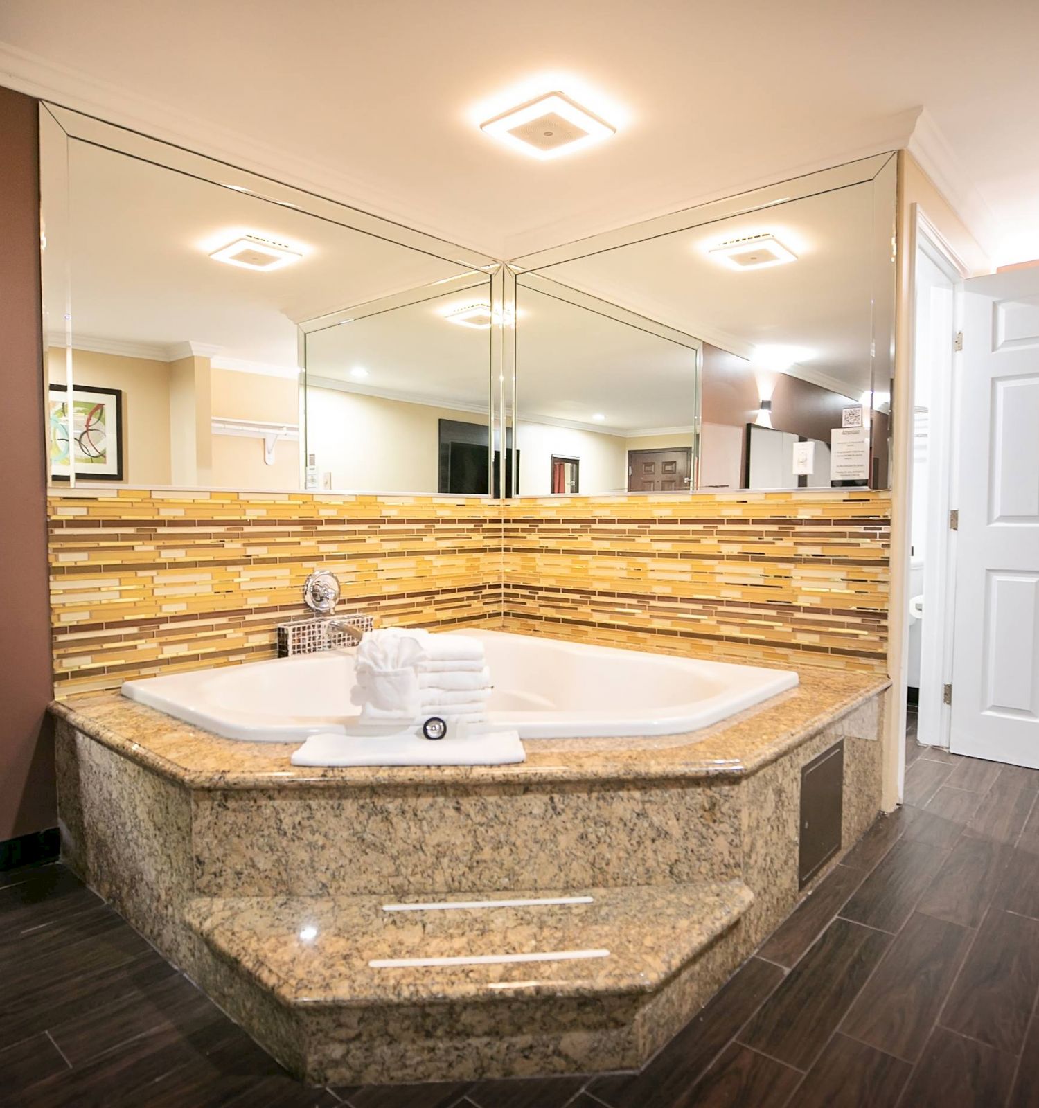 A luxurious bathroom features a jacuzzi tub with mirrors, a tiled backsplash, and neatly folded towels, among modern decor and brown floor tiles.