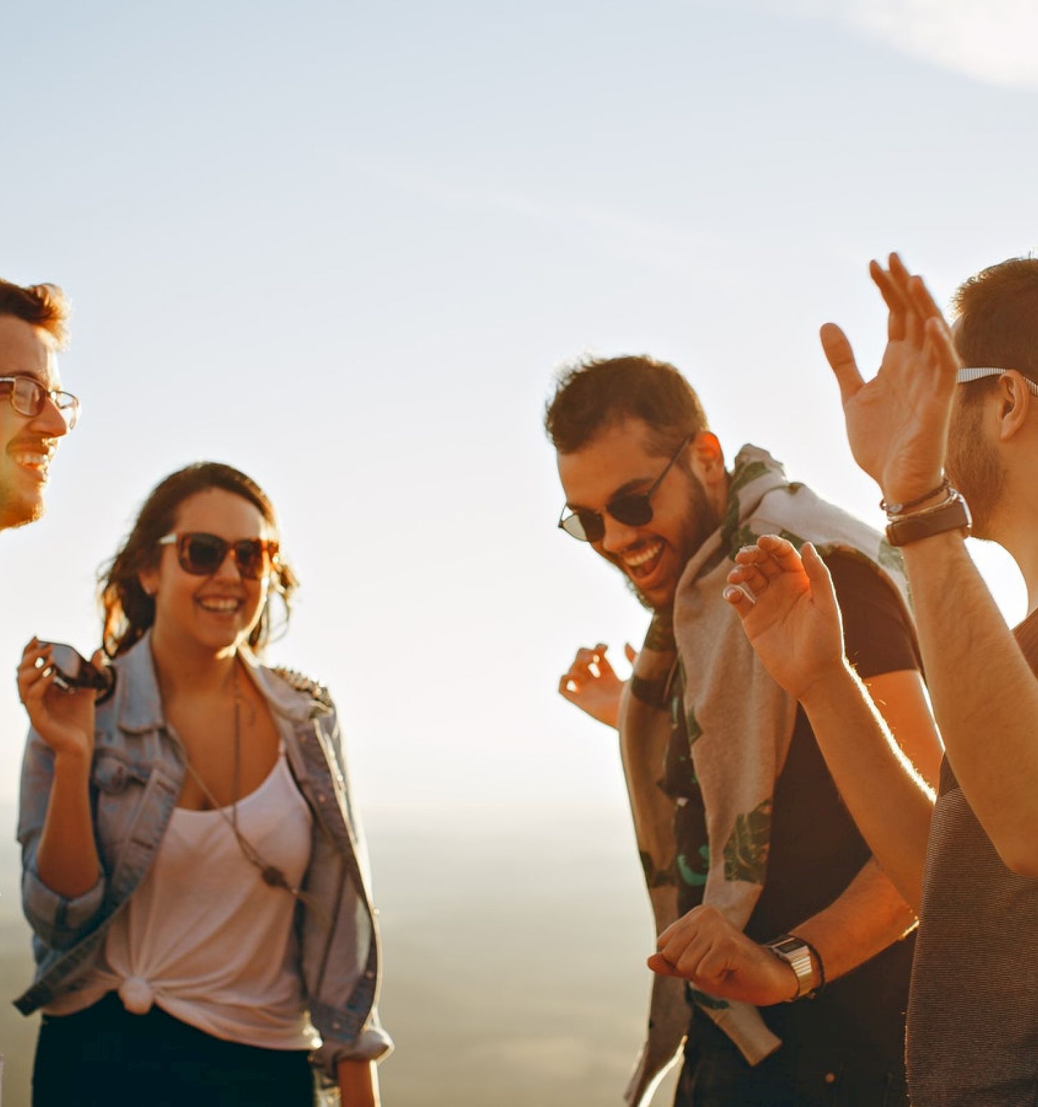 A group of four people are outdoors, enjoying a sunny day, laughing, and interacting with each other. They seem to be having a good time.