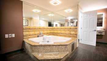 A modern bathroom with a large, corner jacuzzi tub surrounded by mirrors, featuring tile accents and a set of towels on the tub edge.