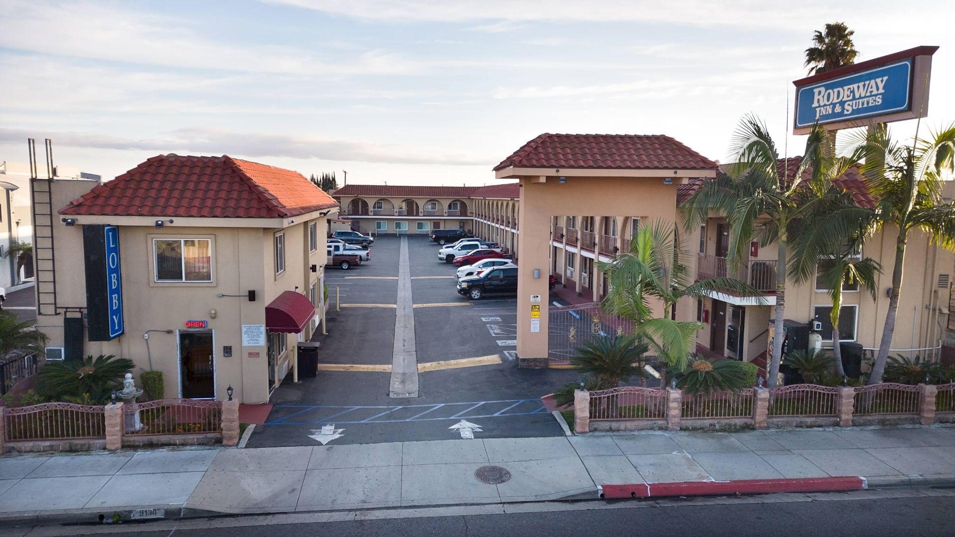This image shows a hotel with a "Rodeway Inn & Suites" sign, parking lot, multiple buildings, and palm trees.