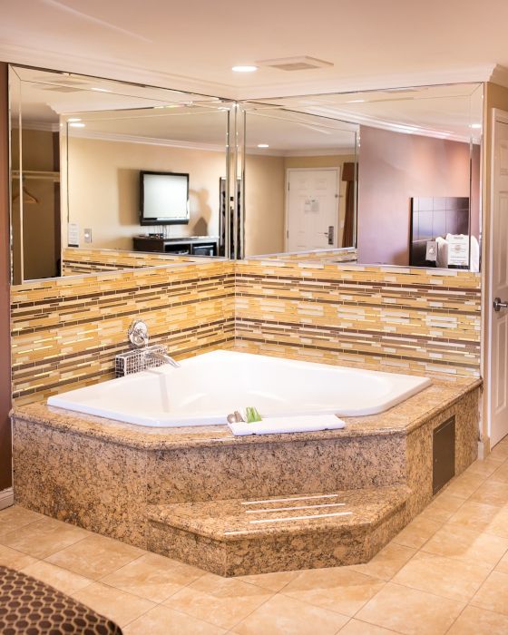 This image shows a luxurious bathroom with a large corner bathtub, surrounded by mirrors and decorated with mosaic tiles, in a spacious setting.